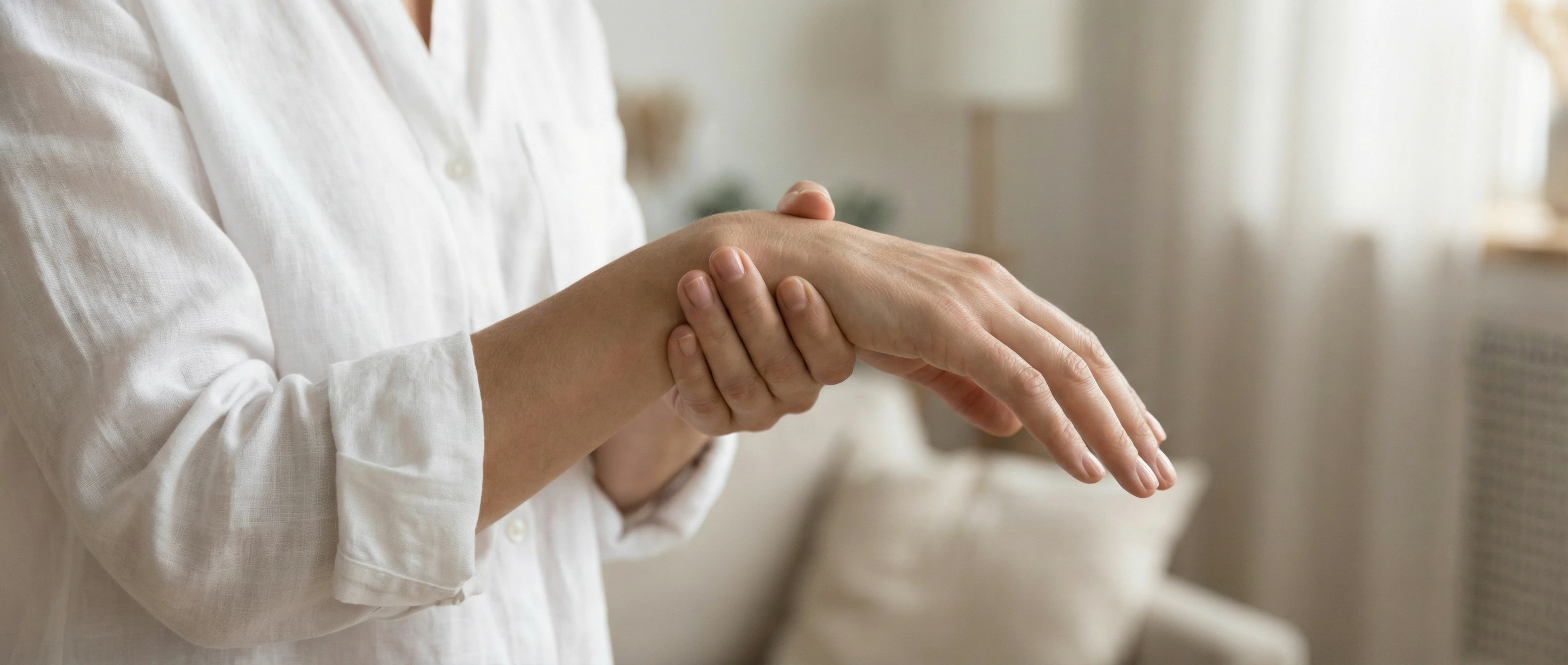 Woman holding her wrist in discomfort at home, experiencing chronic wrist pain from repetitive strain
